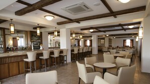 Un vaste espace intérieur comprenant un bar, plusieurs coins salon et un haut plafond avec des poutres apparentes.