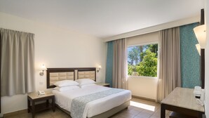 Une chambre d’hôtel avec un lit, une table de chevet avec une lampe, une petite table et une vue sur la verdure.