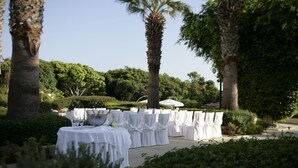 Un espace de restauration en plein air avec des tables recouvertes de nappes blanches et des chaises, entouré de palmiers et de verdure.