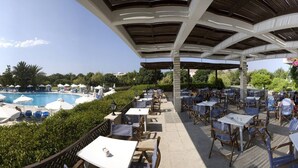 Un espace aménagé au bord de la piscine, avec des chaises longues et des parasols, un coin salon couvert avec des tables et des chaises, et une vue sur la piscine et la végétation environnante.