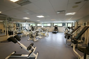 A gym with various exercise machines, mirrors, and windows. - Avanti Hotel (Paphos)