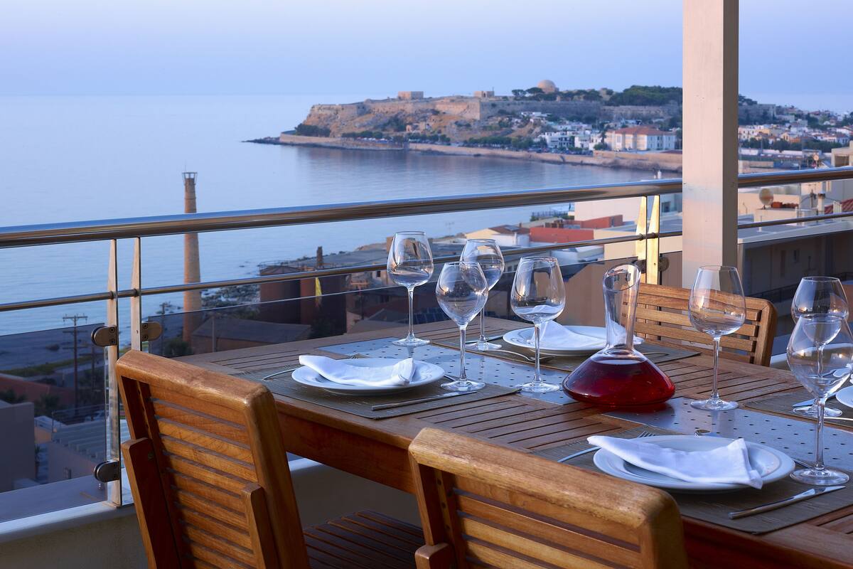 Mesa dispuesta para comer con vista al mar y un fuerte histórico al fondo.