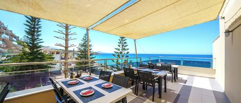 A terrace with tables and chairs, overlooking a coastal view.