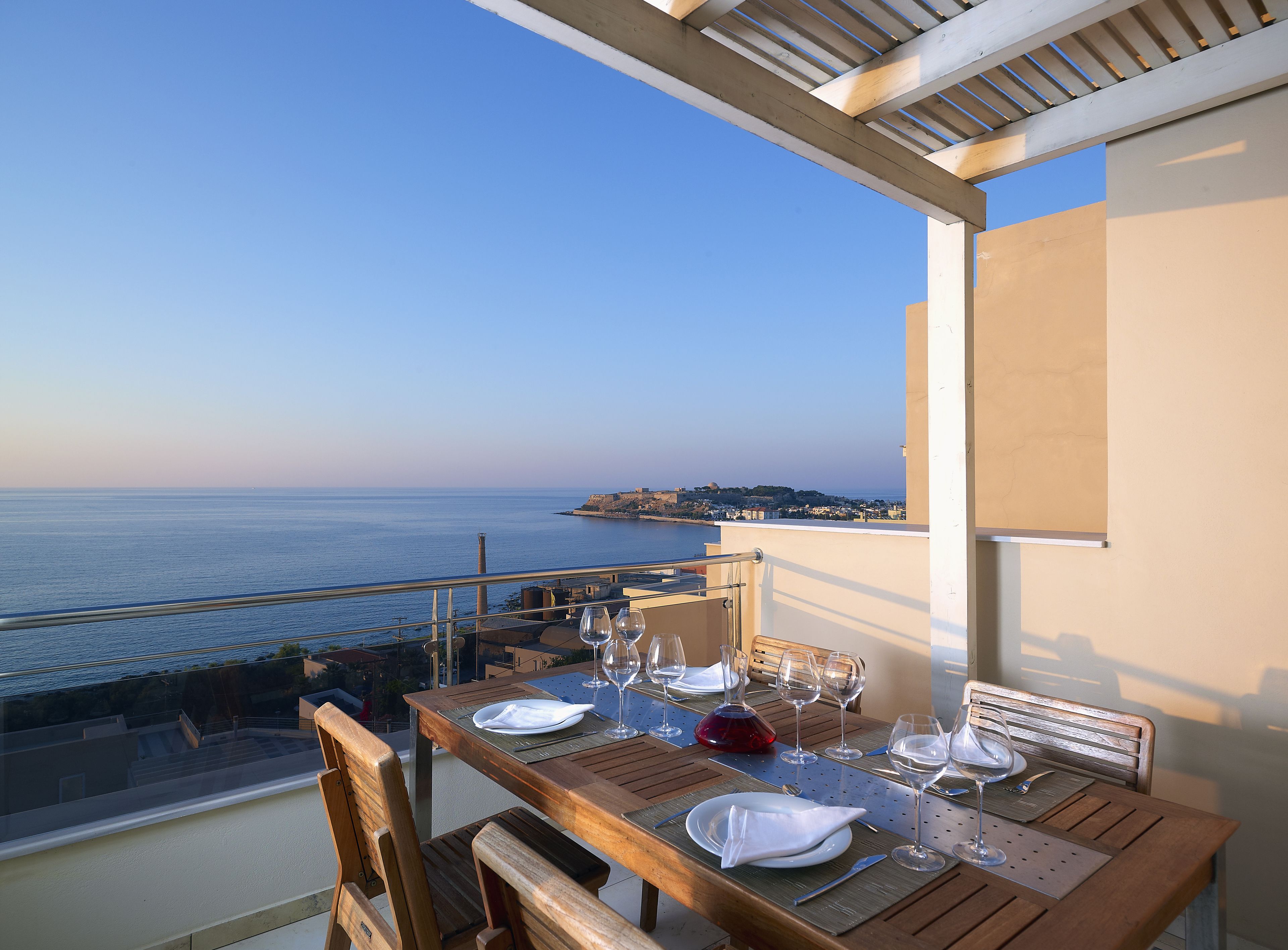 A dining table set for four with wine glasses and plates, overlooking a coastal view.
