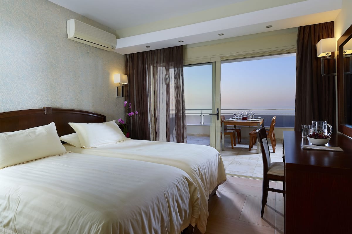 Habitación de hotel con una cama grande, un balcón con mesa y sillas, y vista al horizonte de la ciudad.