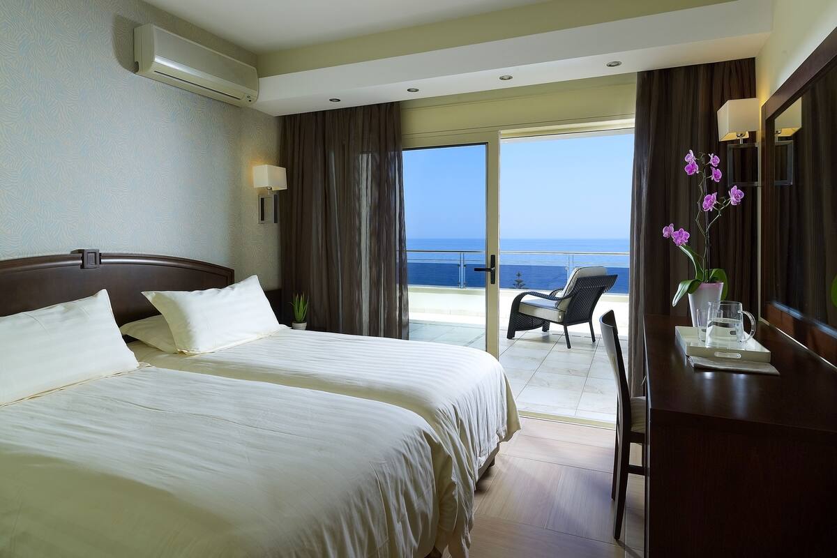 Habitación de hotel con dos camas, un escritorio con una silla, una orquídea en maceta y vistas al mar.