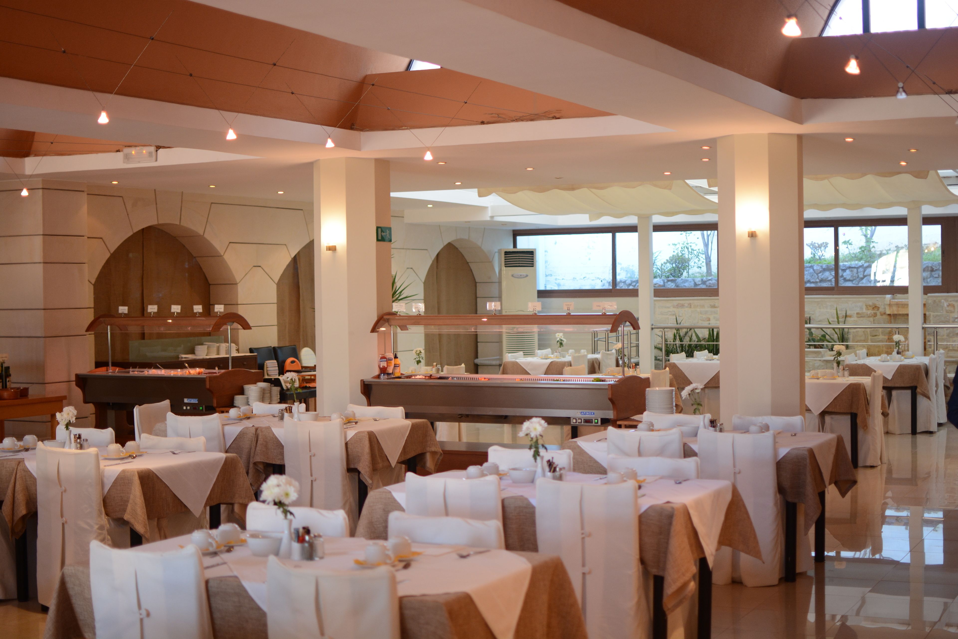 A spacious dining area with multiple tables set for guests, featuring a modern architectural design with large windows and a high ceiling.