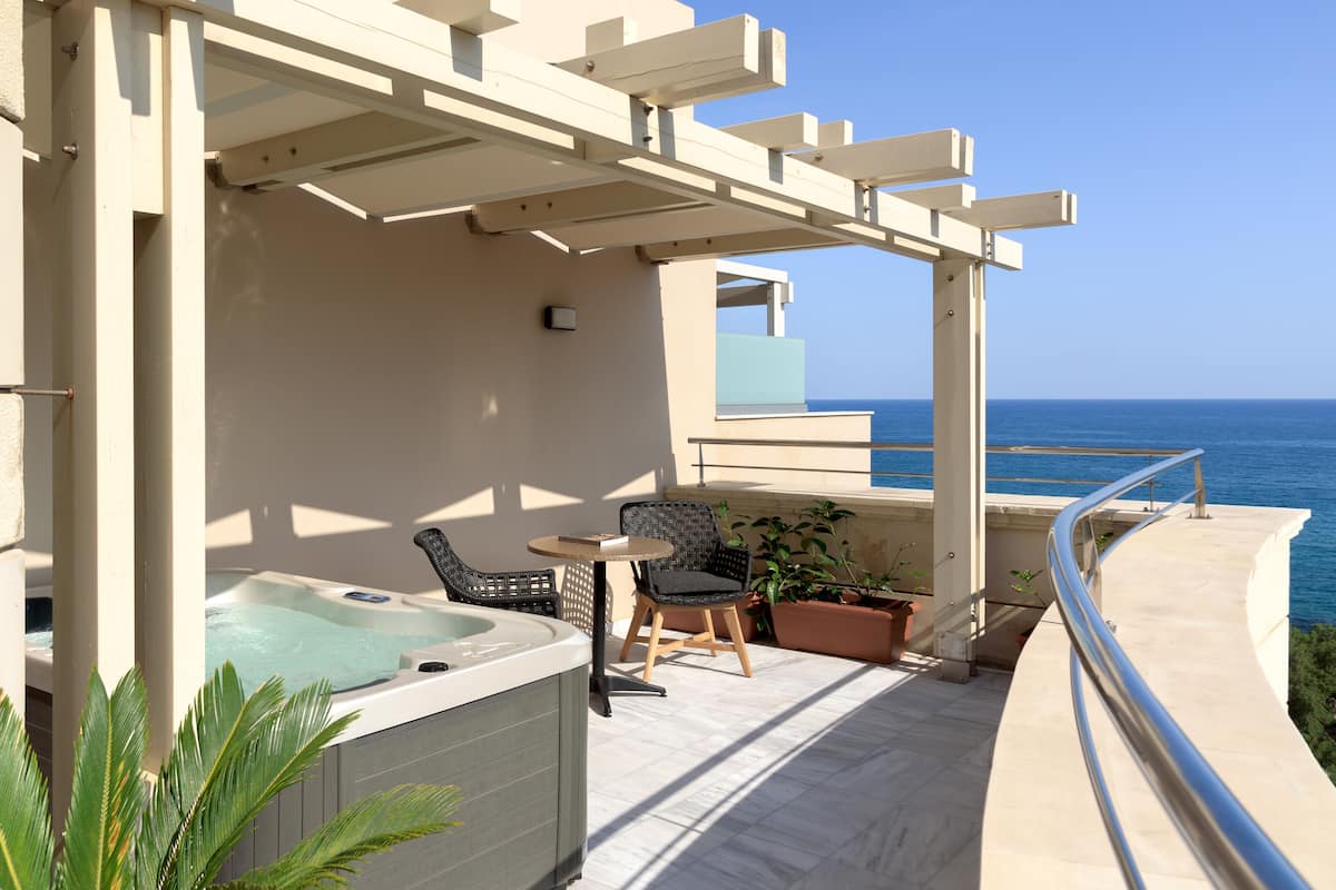 Un balcón con hidromasaje, asientos y vista al mar.