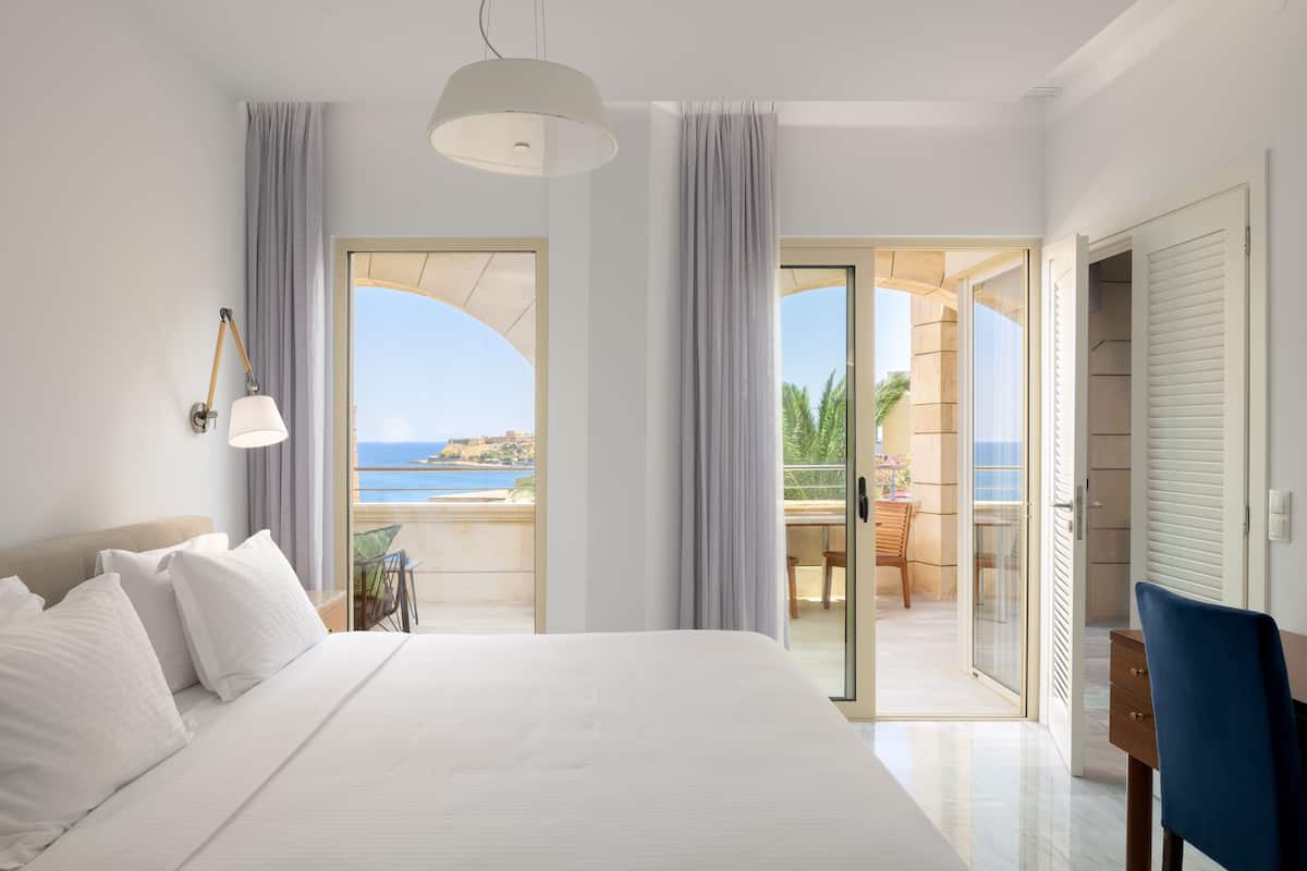 Una habitación de hotel moderna con una cama grande, un escritorio y un balcón con vistas al mar.