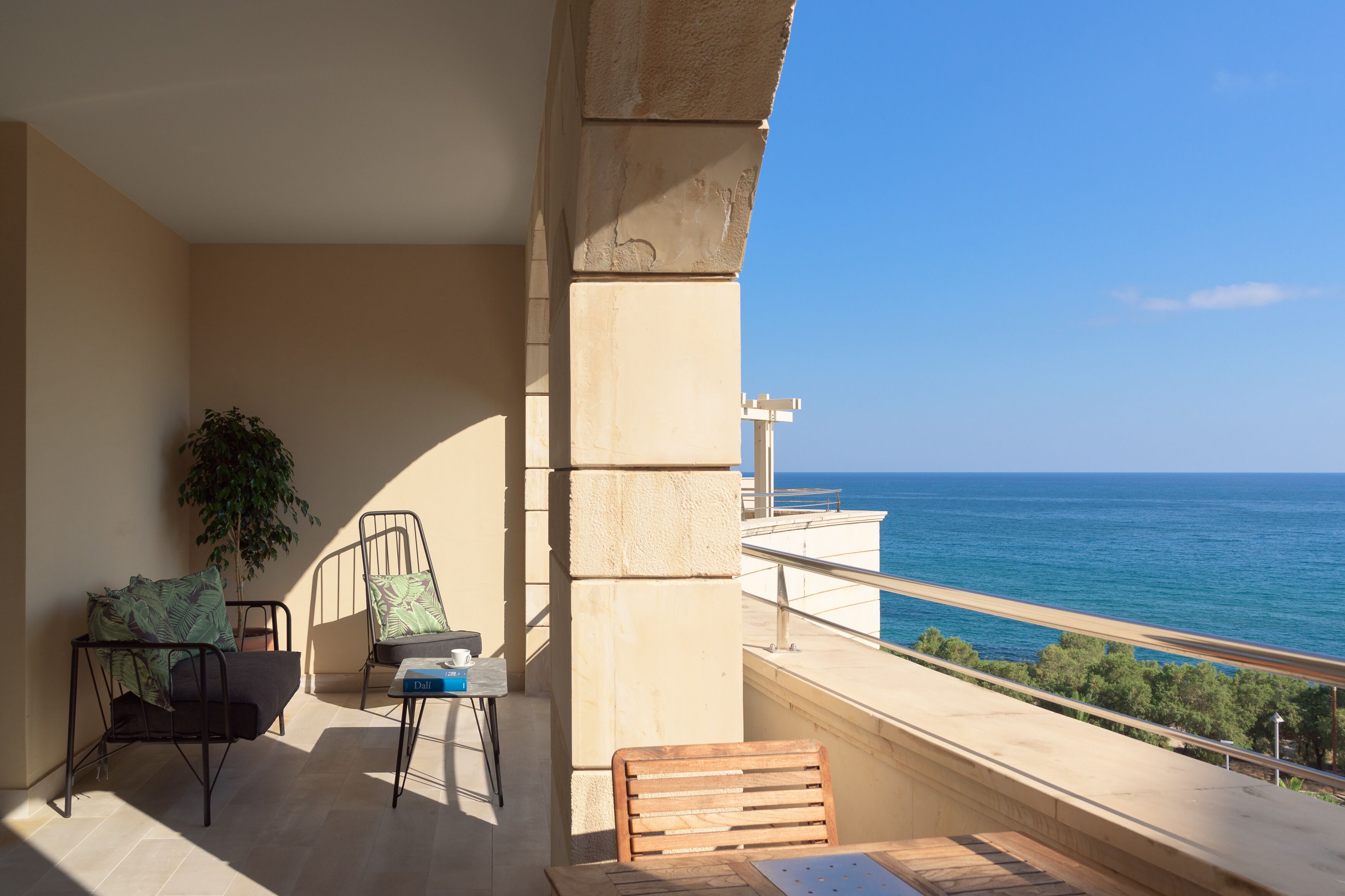 A balcony with a view of the sea, a chair, a table, and a potted plant.