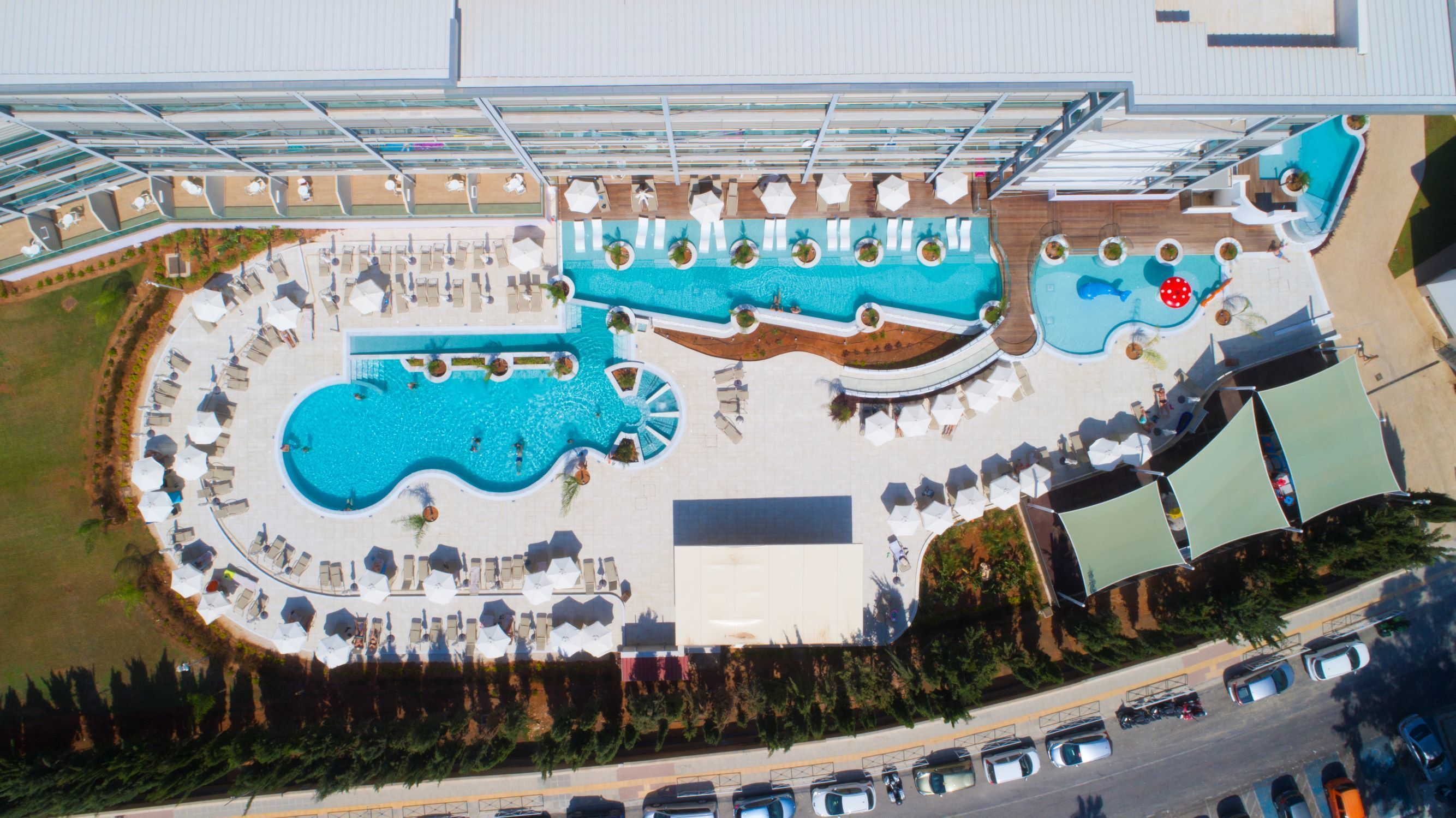 Une vue aérienne d’un complexe hôtelier doté de plusieurs piscines, de chaises longues et d’un espace abrité.