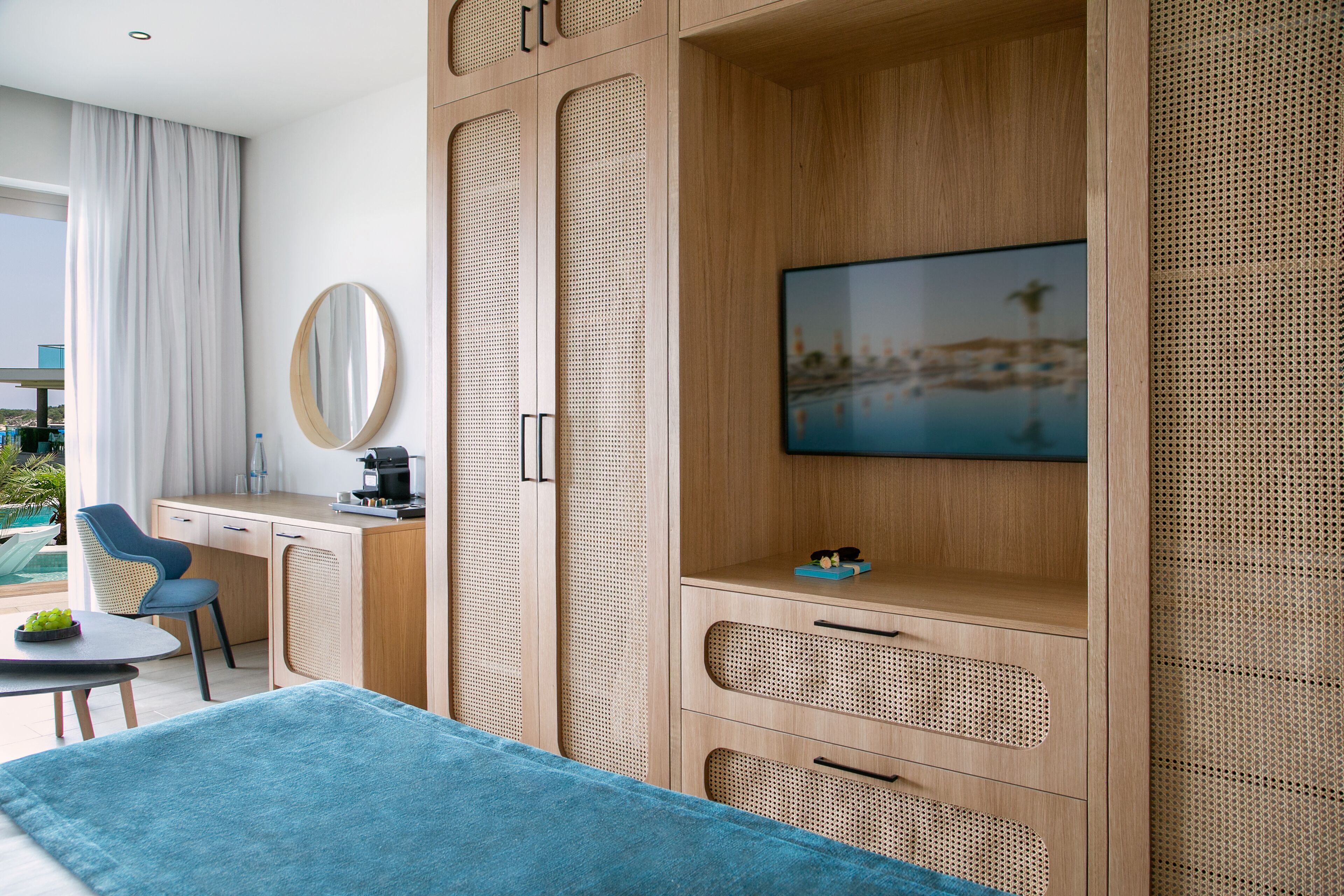 Habitación de hotel moderna con una cama grande, un escritorio, una silla, un televisor montado en una pared de madera y vistas al exterior.