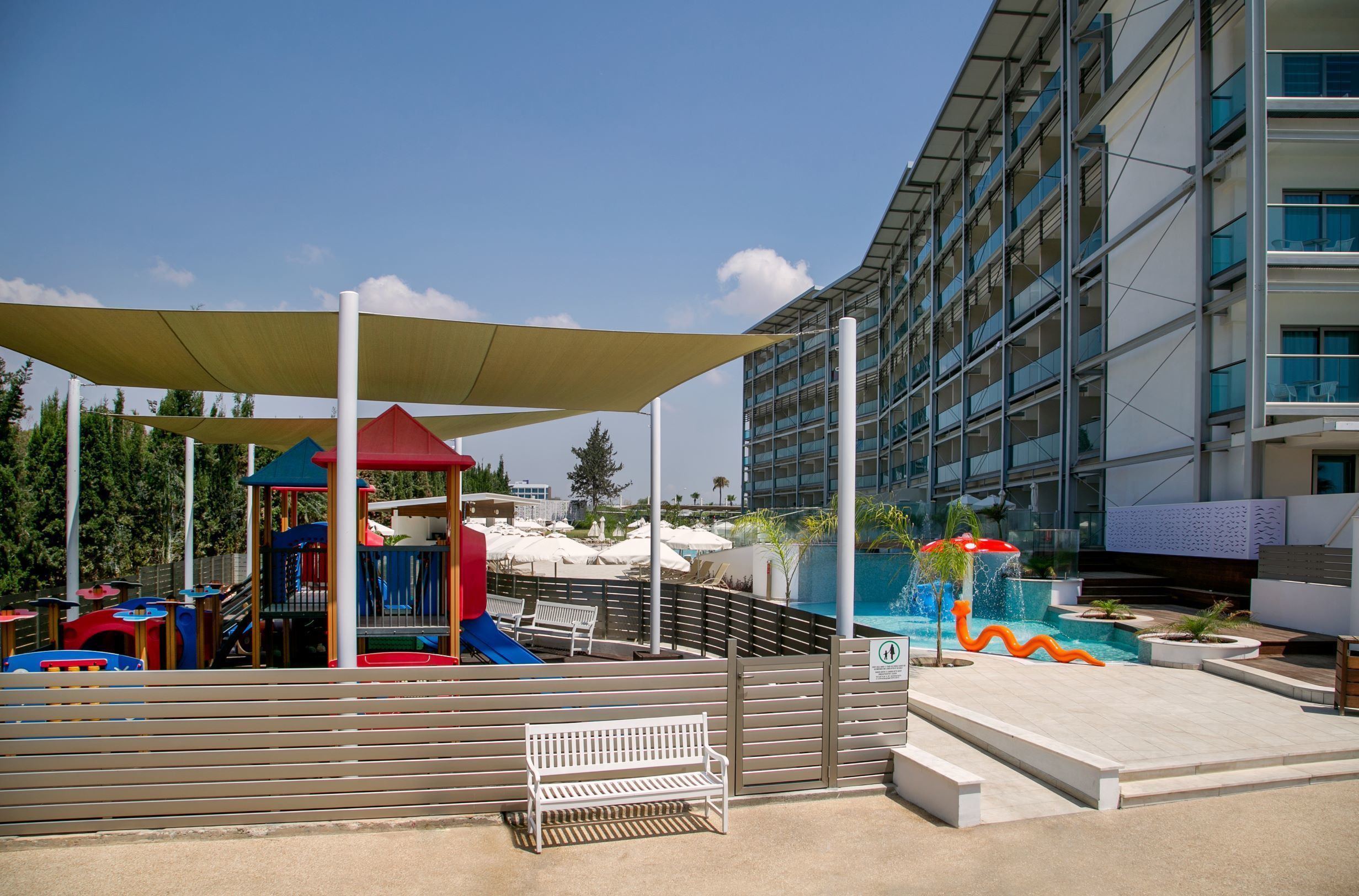 A playground with slides and a playhouse, a pool area with a water feature, and a modern building with balconies.