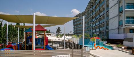 A playground with slides and a playhouse, a pool area with a water feature, and a modern building with balconies.
