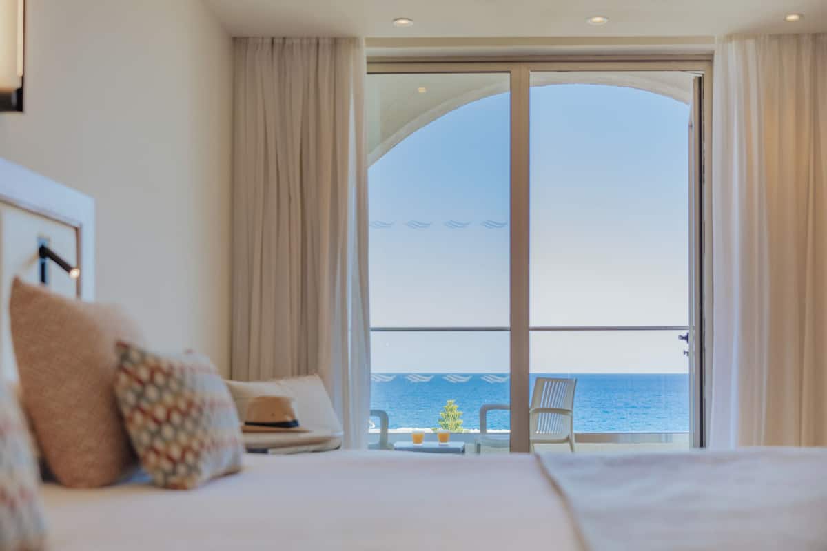 Habitación de hotel con un amplio ventanal corredera que da a un balcón con vista al mar.