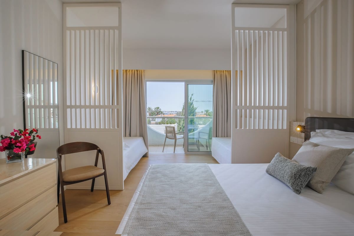 Habitación de hotel con una cama grande, un escritorio, una silla y un balcón con vistas.