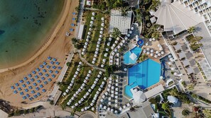 An aerial view of a resort with a beach, multiple pools, and numerous umbrellas. - The Golden Coast Beach Hotel (Paralimni)