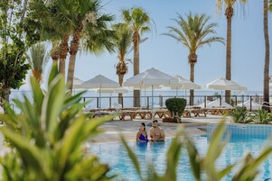 A pool area with lounge chairs and umbrellas, surrounded by palm trees.
