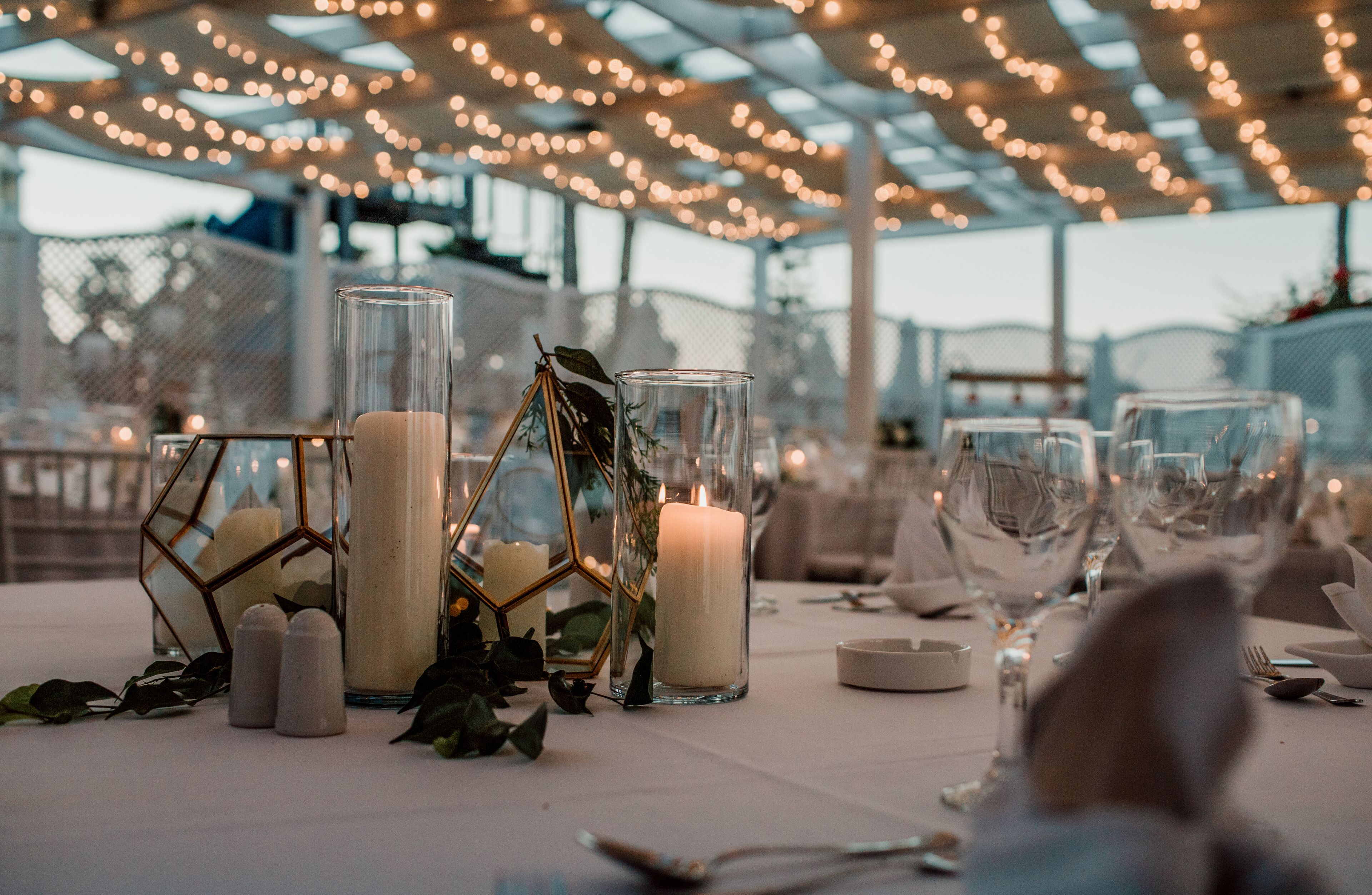 Una mesa dispuesta para un evento formal, con velas, cristalería y candelabros geométricos de vidrio.