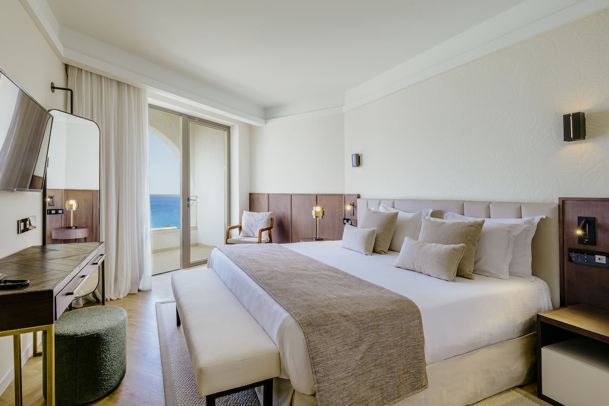 Habitación de hotel con una cama grande, un escritorio, una silla y vista al mar.