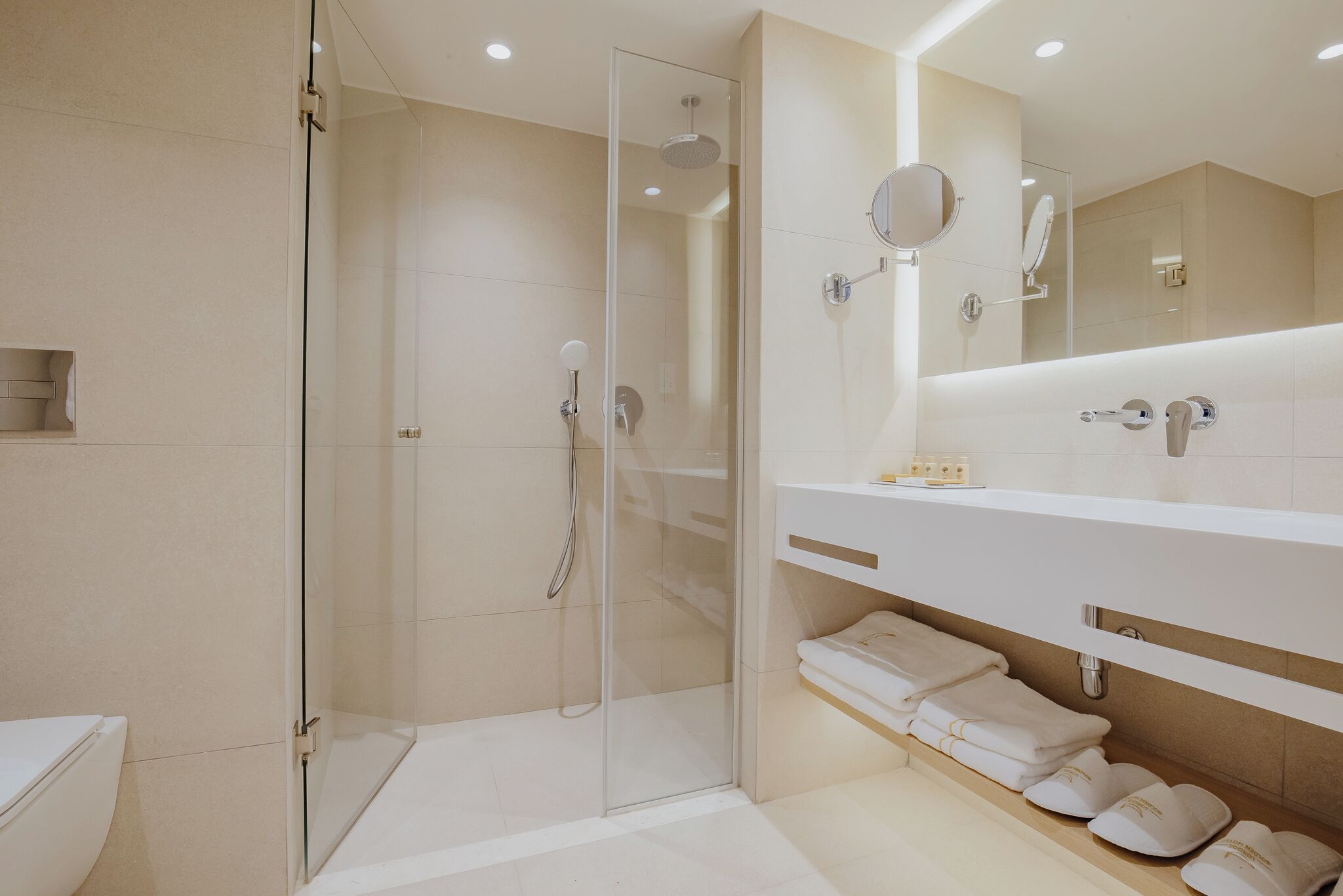 A modern bathroom with a glass-enclosed shower, a white sink with a mirror, and neatly folded towels.