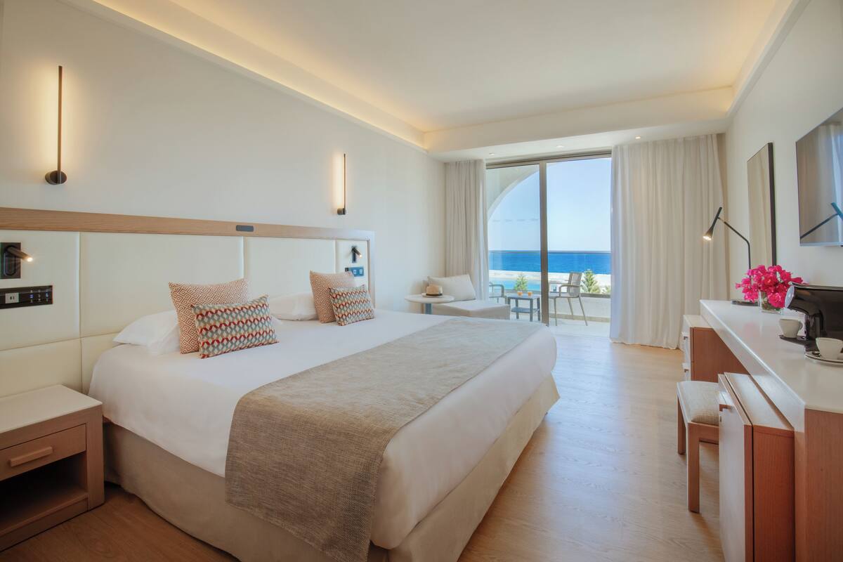 Habitación de hotel moderna con una cama grande, mesitas de noche, un escritorio y vista al océano.