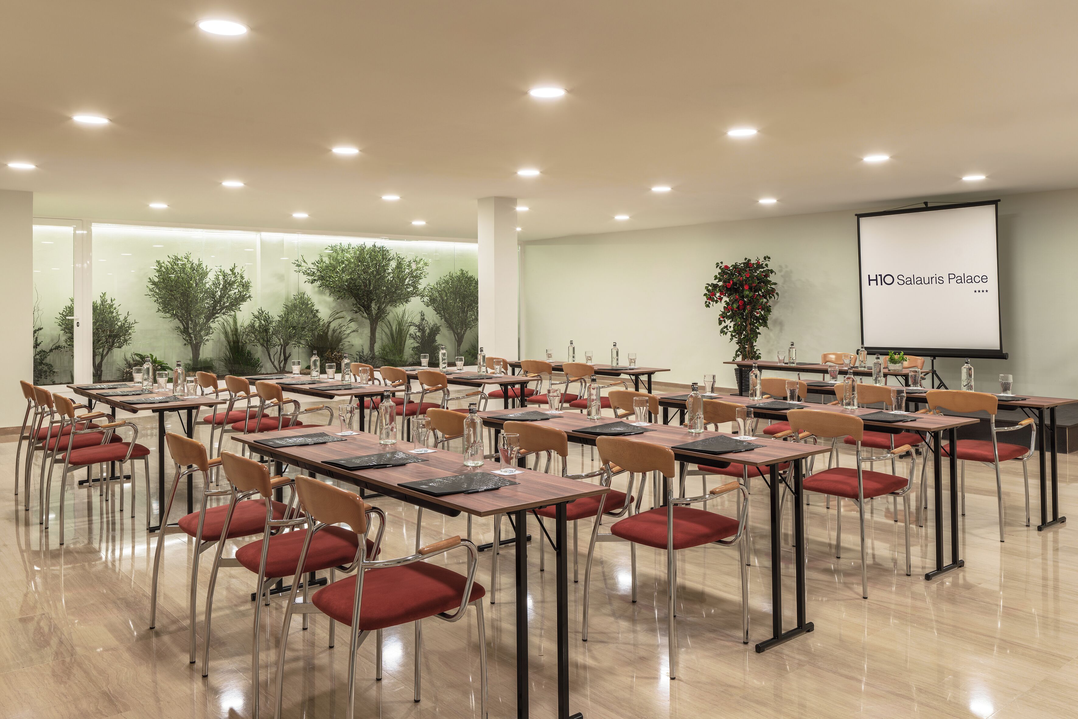 A conference room with tables, chairs, and a projector screen displaying 'H10 Salauris Palace'.