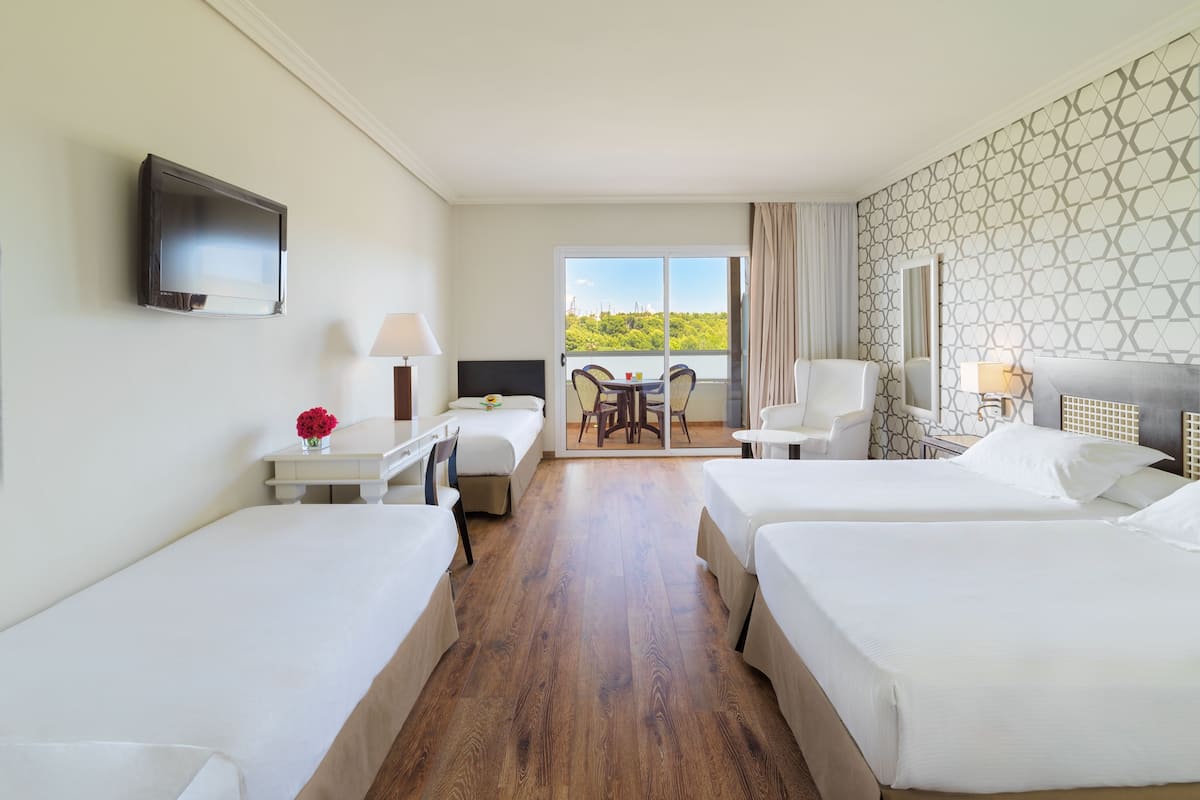 Ein Hotelzimmer mit zwei Betten, einem Schreibtisch, einem Stuhl, einem Fernseher und einem Balkon mit Blick.
