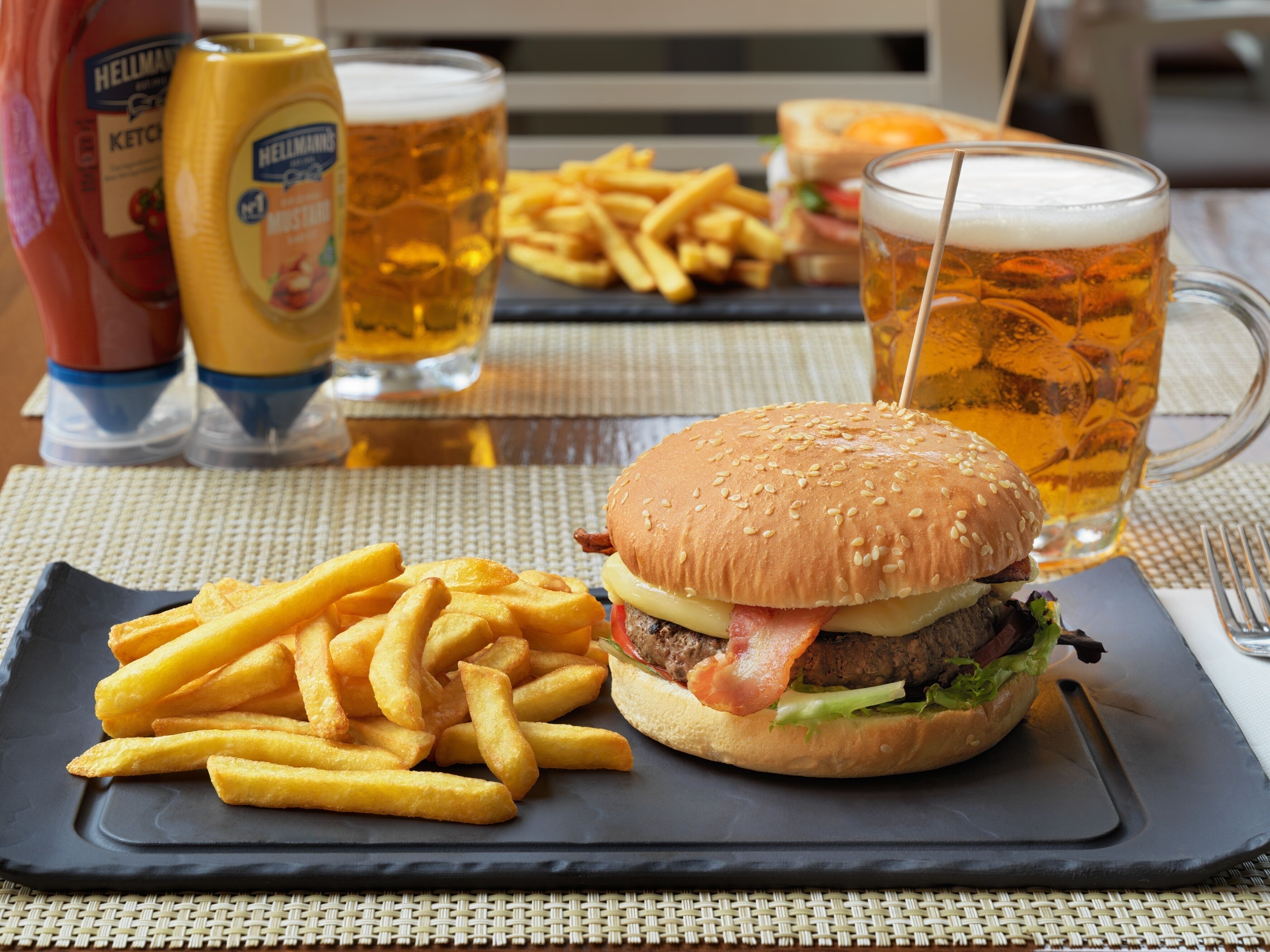 Ein Essen bestehend aus einem Burger, Pommes und zwei Bieren auf einem Tisch.