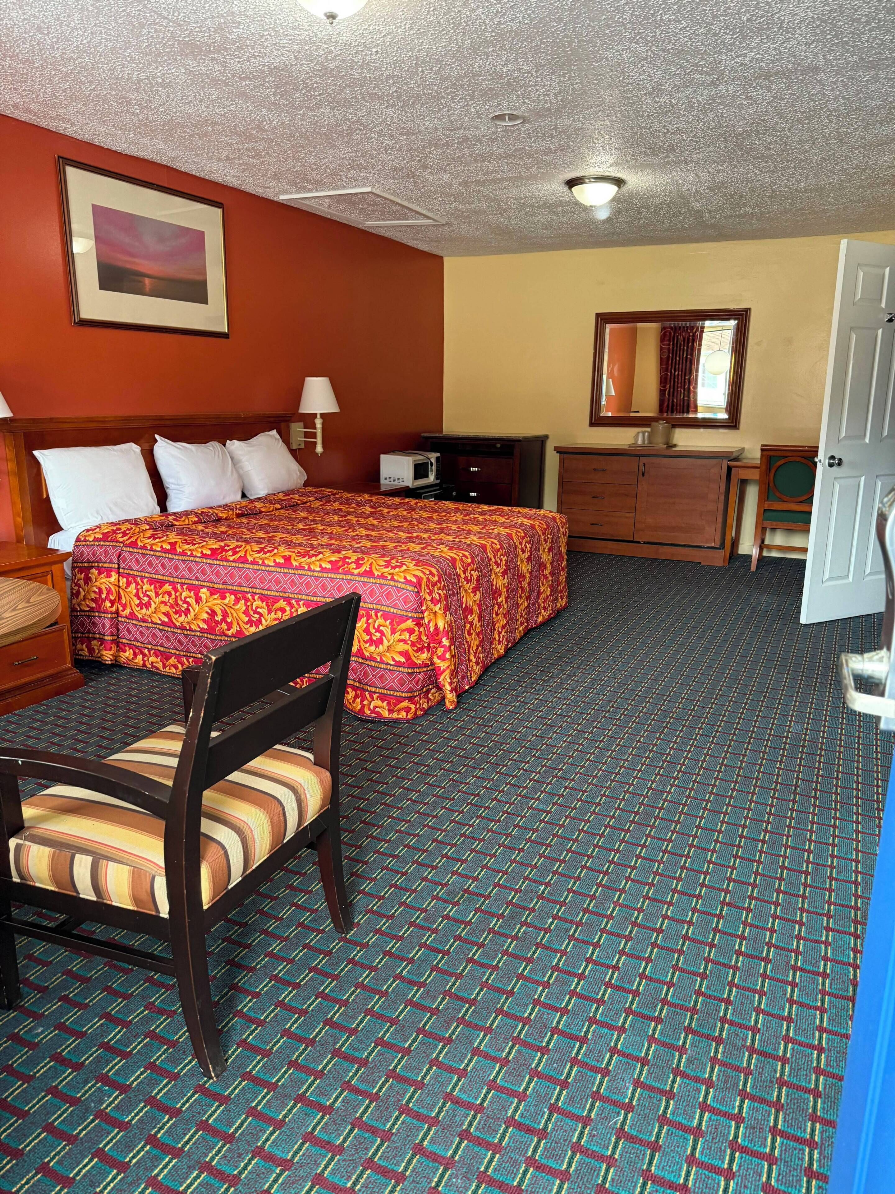 Une chambre d’hôtel équipée d’un lit, d’une chaise, d’un bureau, d’un four à micro-ondes, d’une commode et d’un miroir.