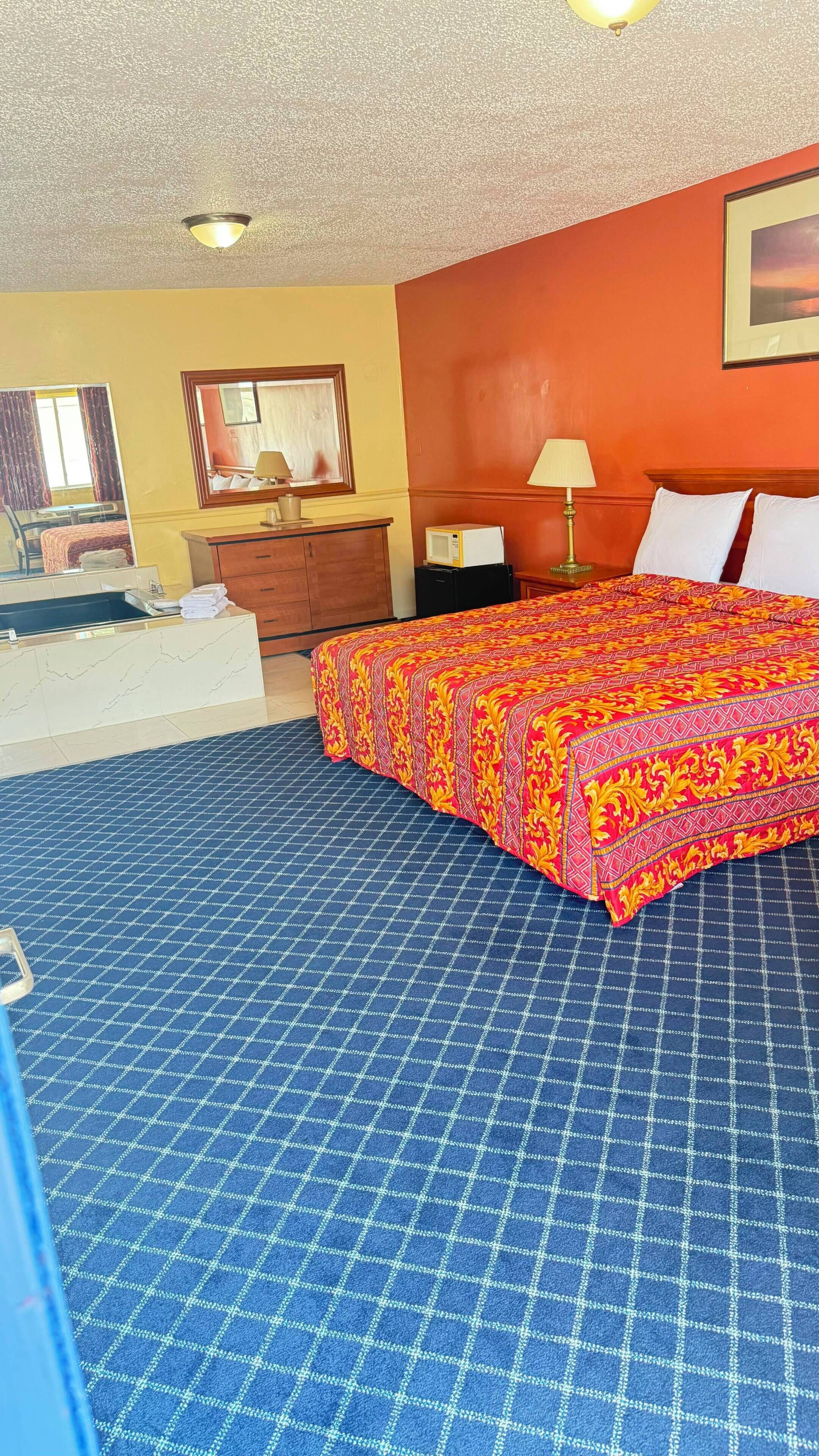 A hotel room with a bed, a desk, a chair, a lamp, and a mirror.