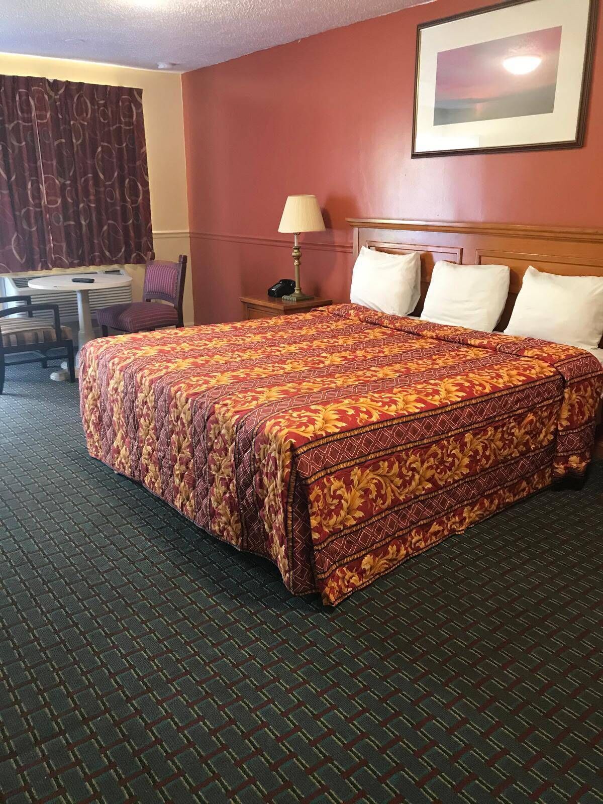 A hotel room with a large bed, a desk with a chair, a lamp, and a framed picture on the wall.