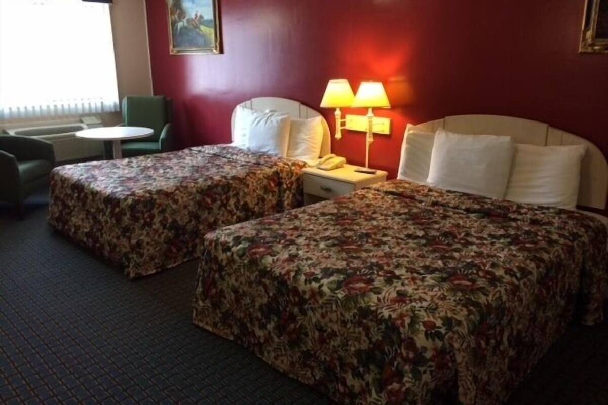 A hotel room with two beds, a desk, a chair, a lamp, and a painting on the wall.