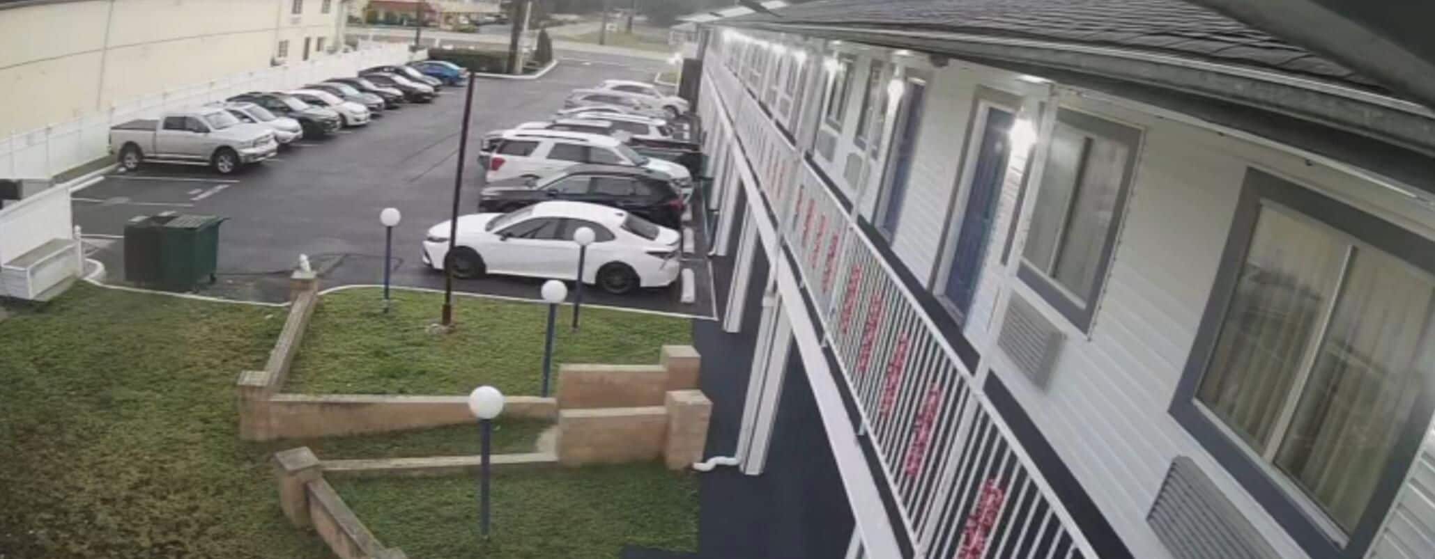 Un parking avec plusieurs voitures et un immeuble doté d’un balcon.
