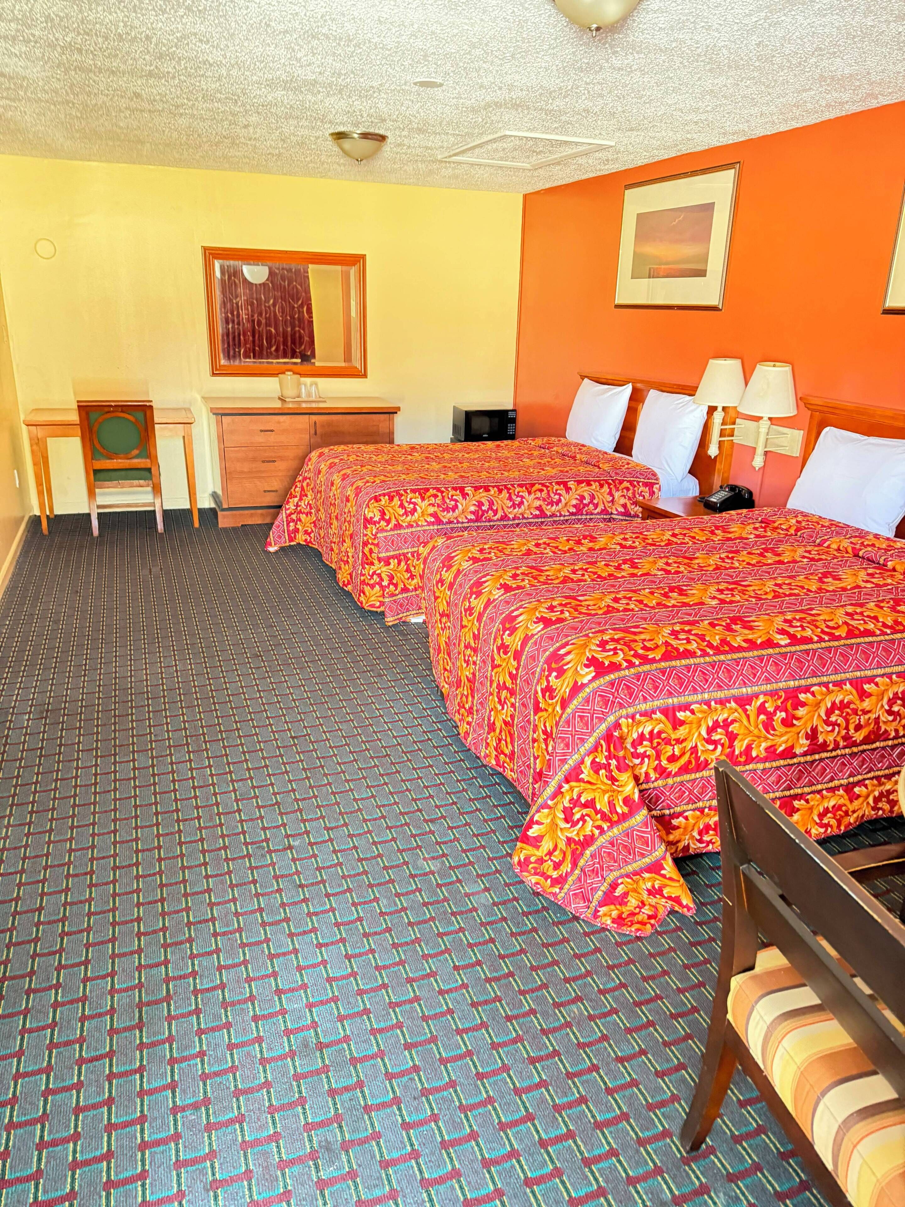 A hotel room with two beds, a desk, a chair, and a small table.