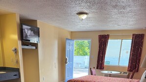 A hotel room with two beds, a TV, a bathroom, and a view of the outside.