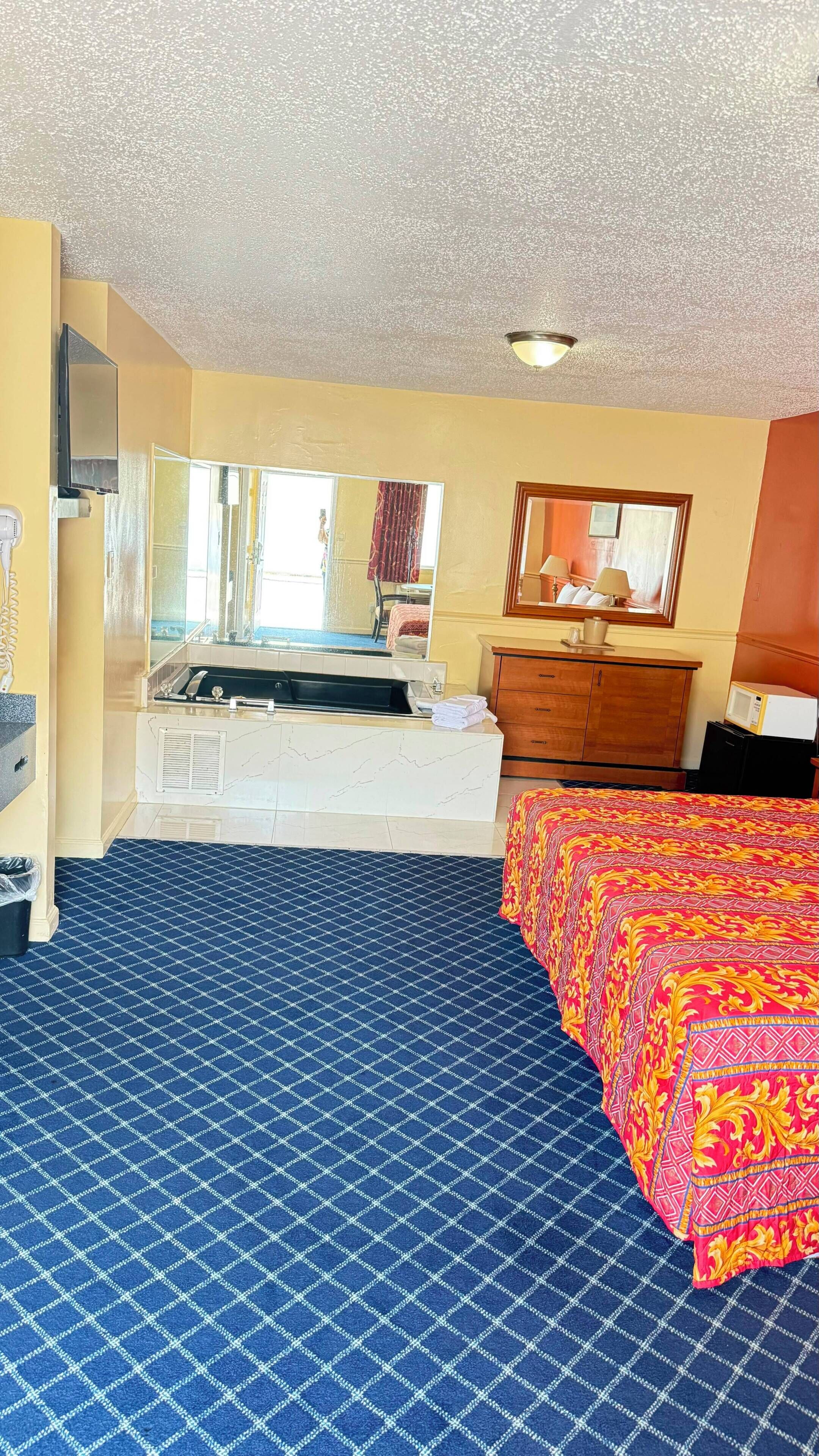 A hotel room with a bed, a dresser, a mirror, a sink, and a television.