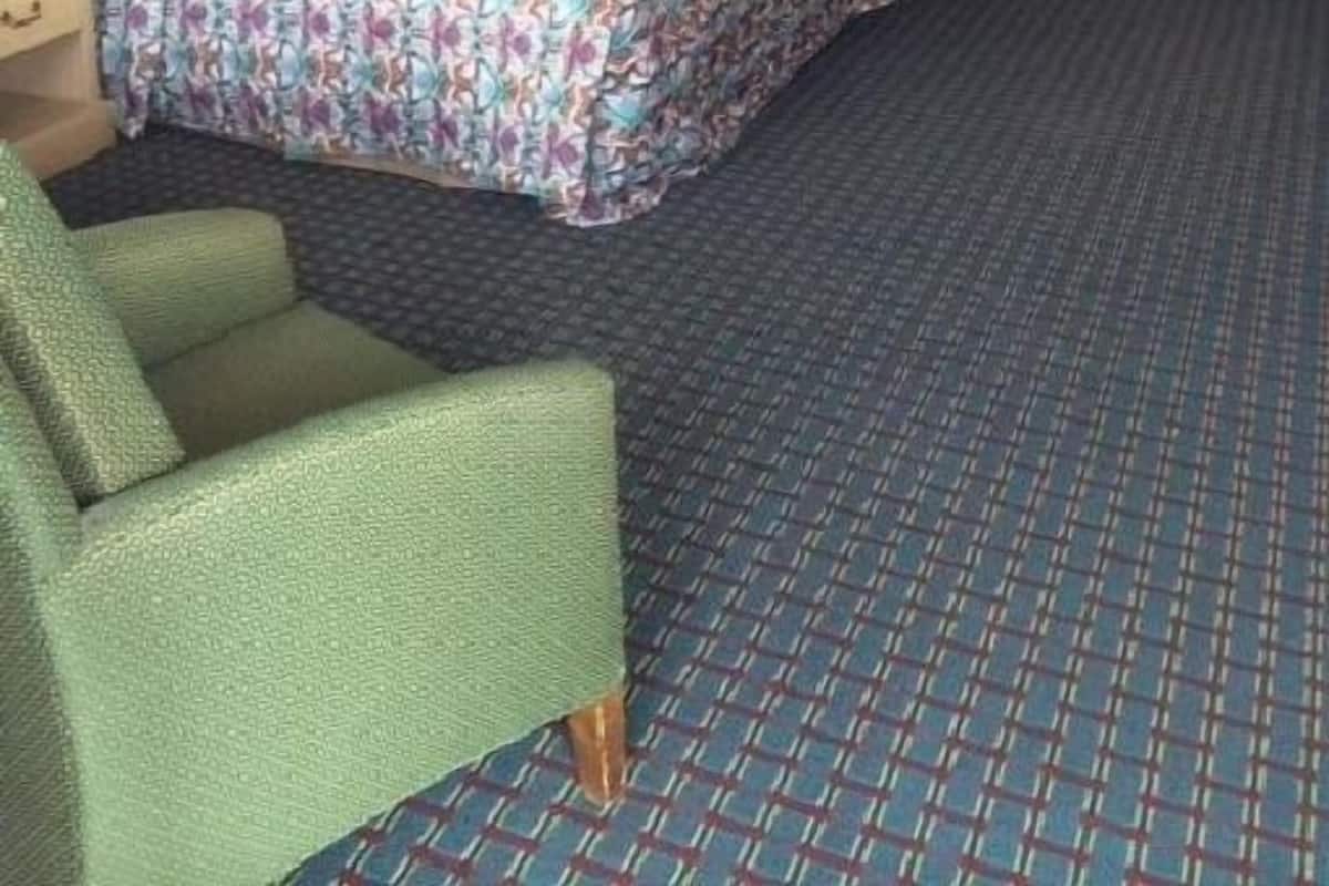 A hotel room with a bed, a chair, a dresser, a mirror, and a ceiling fan.