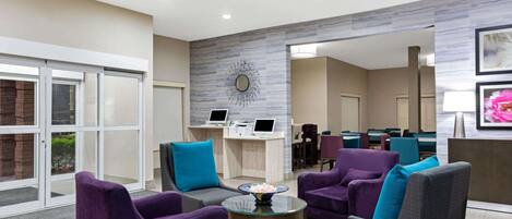 Een moderne lobby met paarse en grijze fauteuils, een glazen bijzettafeltje en een receptiebalie met computers.