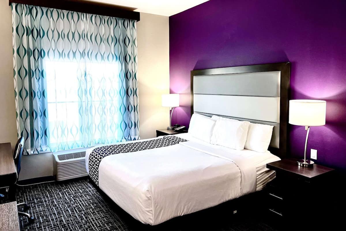 Une chambre d’hôtel avec un lit, deux lampes de chevet, une fenêtre avec des rideaux à motifs et un radiateur mural.