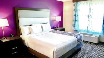 Habitación de hotel con una cama grande, dos mesitas de noche y un equipo de aire acondicionado. Cuenta con una ventana con cortinas.