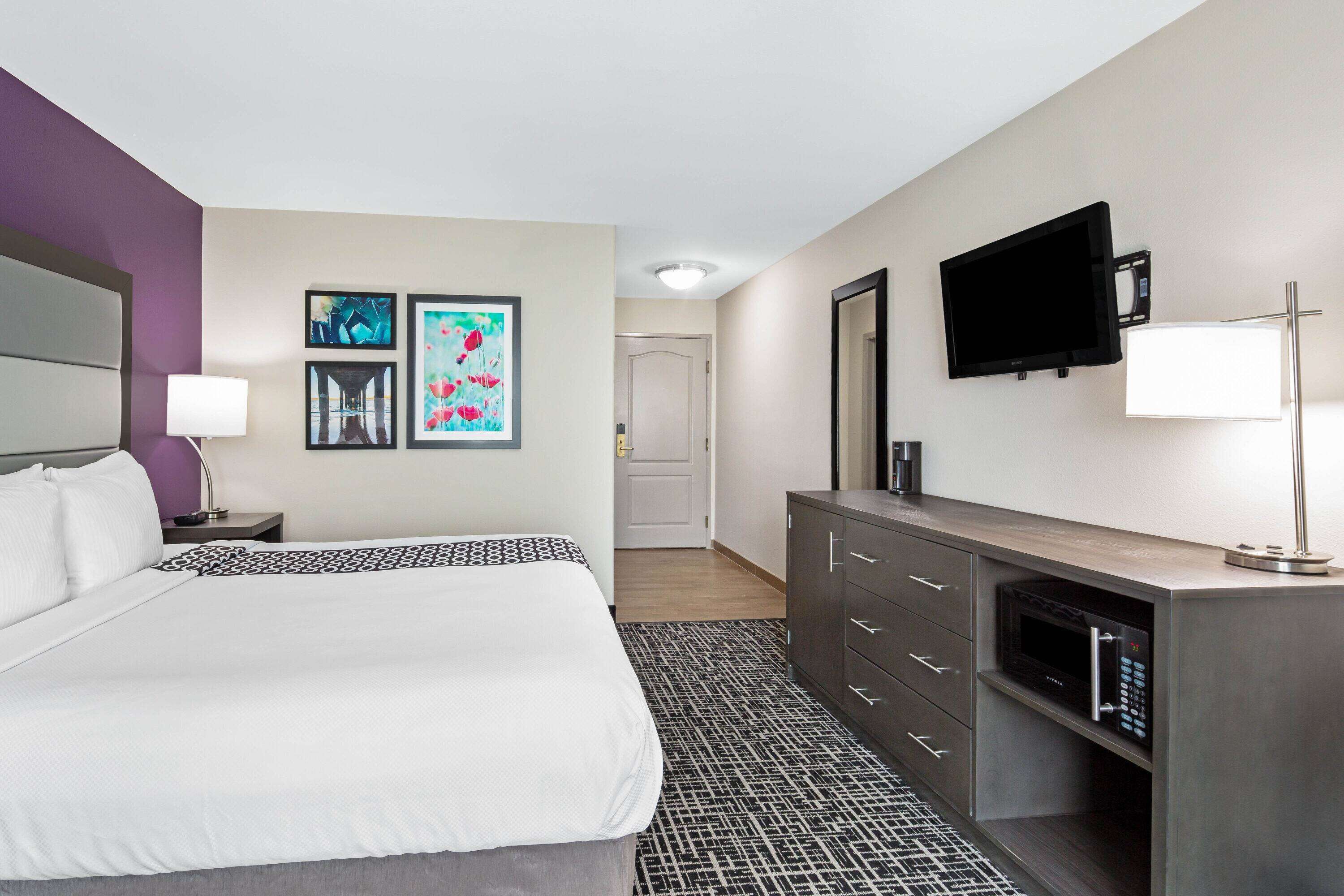 Ein Hotelzimmer mit einem Bett, einem Schminktisch, einem Fernseher und Bildern an der Wand.