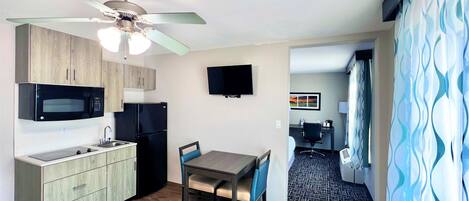 A compact kitchen with modern appliances, a dining area with a table and chairs, and a ceiling fan.