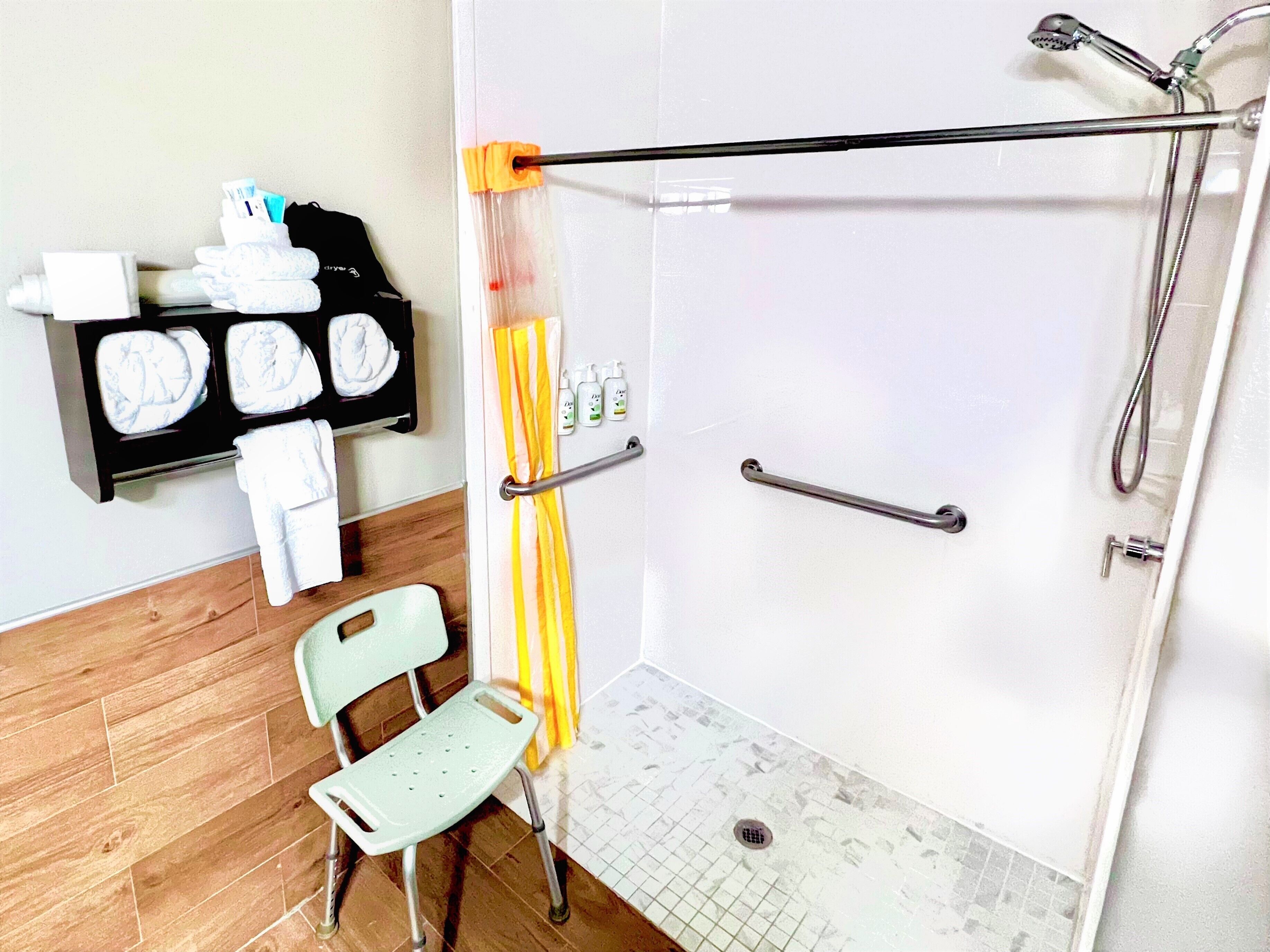 A shower area with a grab bar, a chair, and a shelf with towels and toiletries.