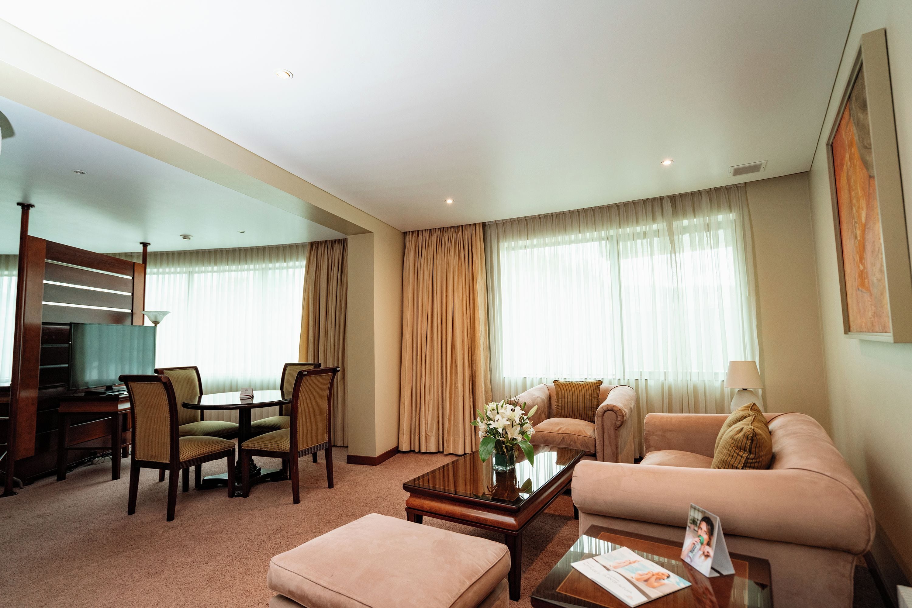 Habitación de hotel con sala de estar, una mesa de comedor con sillas, un sofá, una mesa baja y un televisor.