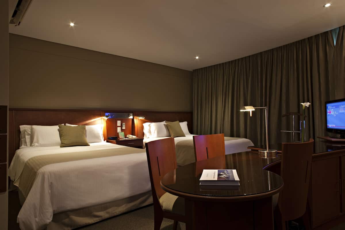 A hotel room with two beds, a desk, a chair, a television, and a lamp.