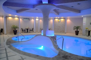 Una piscina interior con una columna central, zona de estar y plantas en macetas.