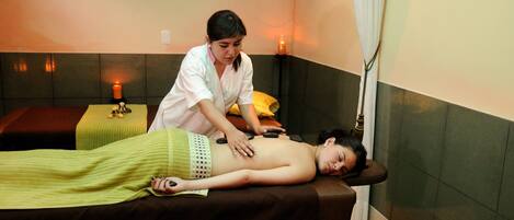 A massage therapy room with a massage table, candles, and a person receiving a back massage.