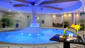 Piscina con una fuente central, rodeada de sillas de descanso y mesas, y un área de comedor con comida y bebidas.