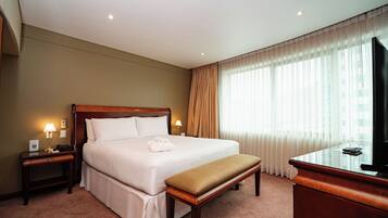 A hotel room with a large bed, bedside lamps, a desk with a telephone, a television, and a window with sheer curtains.